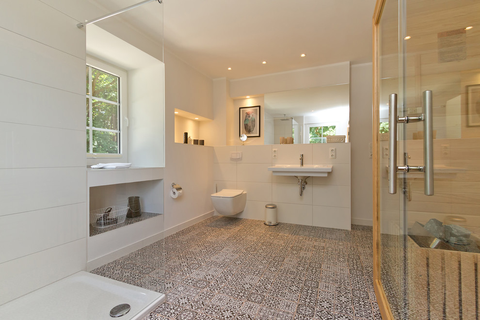 This is an example of a large contemporary bathroom in Berlin with a corner shower, a wall-mount toilet, white tile, ceramic tile, white walls, cement tiles, with a sauna, a wall-mount sink and multi-coloured floor.