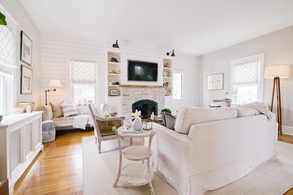 This is an example of a large traditional open concept living room in Providence with white walls, medium hardwood floors, a wood stove, a stone fireplace surround, a built-in media wall and beige floor.
