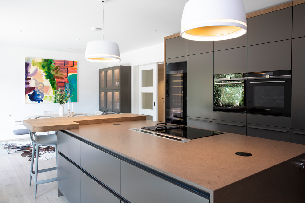 Contemporary eat-in kitchen in Sussex with flat-panel cabinets, grey cabinets, black appliances, light hardwood floors, with island and grey benchtop.