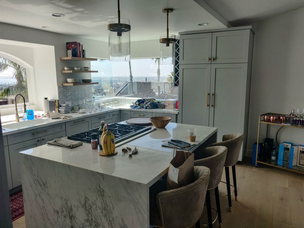 Photo of a large midcentury u-shaped open plan kitchen in San Diego with a submerged sink, shaker cabinets, grey cabinets, marble worktops, white splashback, marble splashback, stainless steel appliances, light hardwood flooring, an island, beige floors and white worktops.