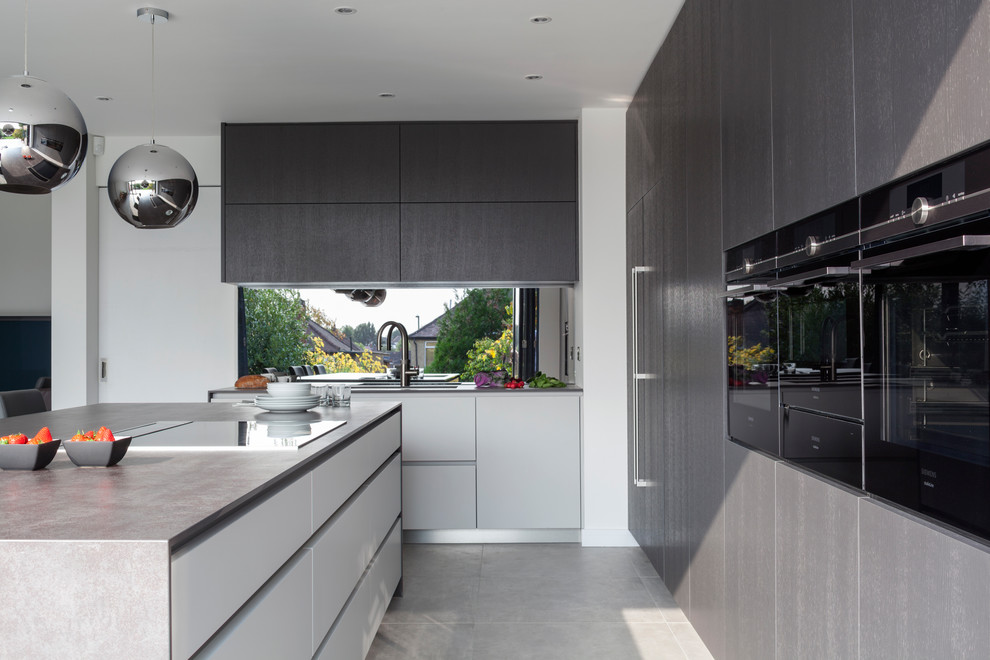 Expansive modern l-shaped open plan kitchen in London with flat-panel cabinets, a peninsula, an integrated sink, brown cabinets, brown splashback, mirror splashback and stainless steel appliances.
