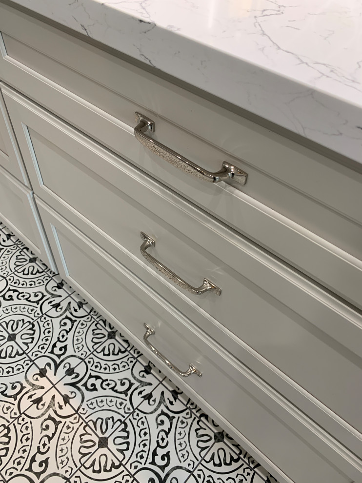 Transitional l-shaped porcelain tile and multicolored floor kitchen photo in Houston with a farmhouse sink, recessed-panel cabinets, white cabinets, quartz countertops, gray backsplash, ceramic backsplash, stainless steel appliances, an island and white countertops