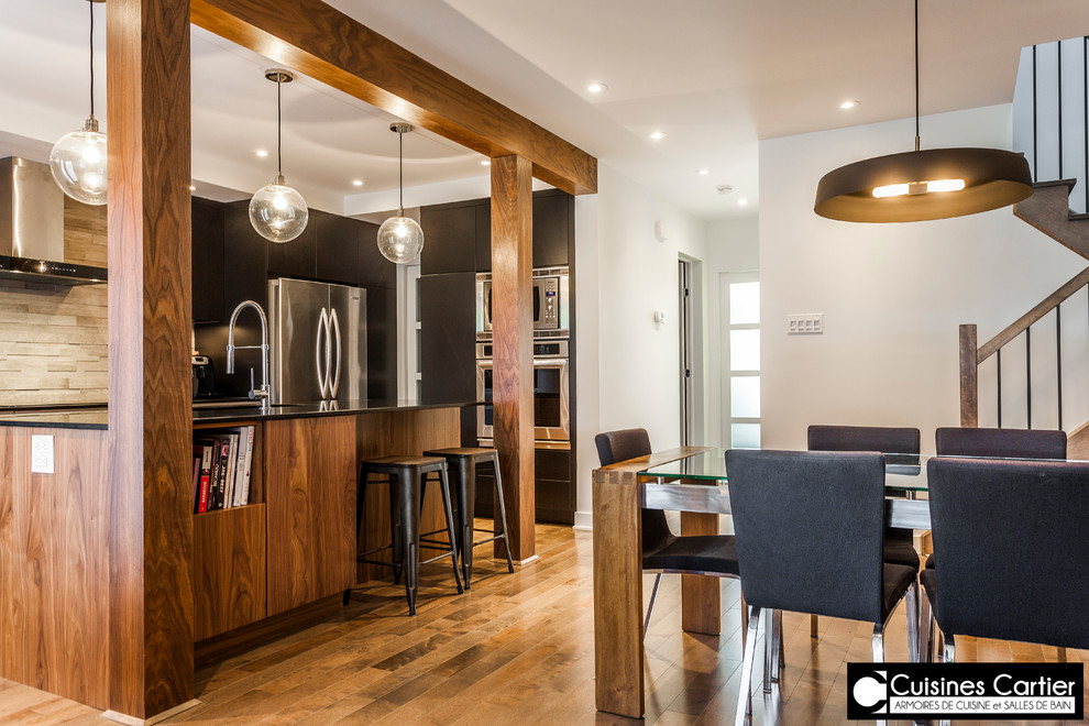 This is an example of a mid-sized contemporary galley kitchen pantry in Montreal with an integrated sink, flat-panel cabinets, black cabinets, quartzite benchtops, grey splashback, stone tile splashback, stainless steel appliances, medium hardwood floors and with island.