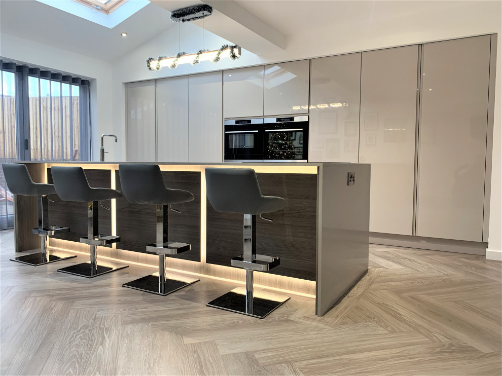 This is an example of a mid-sized contemporary single-wall eat-in kitchen in Other with a single-bowl sink, flat-panel cabinets, quartzite benchtops, black appliances, vinyl floors, with island and beige benchtop.
