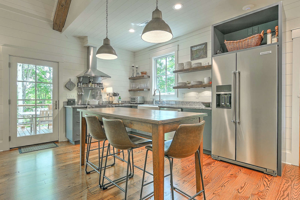 This is an example of a small country l-shaped eat-in kitchen in Other with a farmhouse sink, flat-panel cabinets, grey cabinets, granite benchtops, shiplap splashback, stainless steel appliances, medium hardwood floors, no island, grey benchtop and timber.