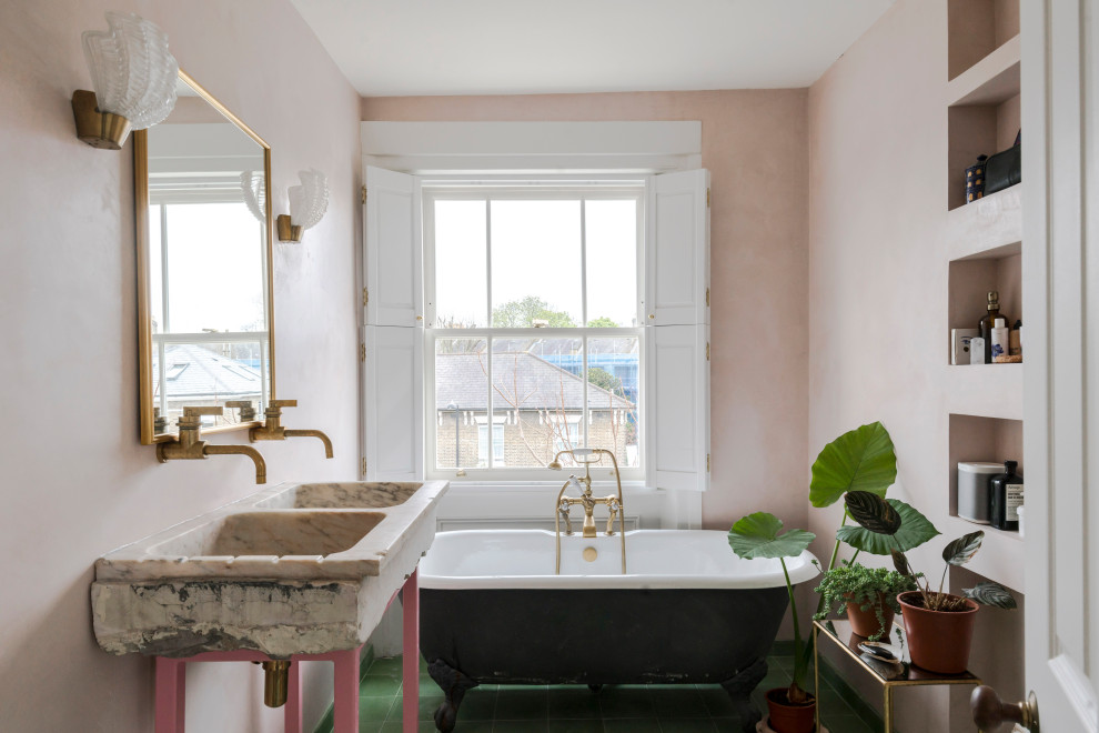Design ideas for an eclectic bathroom in London with a claw-foot tub, pink walls, a console sink, green floor and a double vanity.