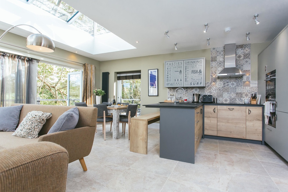 This is an example of a country u-shaped open plan kitchen in Cambridgeshire with flat-panel cabinets, light wood cabinets, grey splashback, a peninsula, grey floor and black benchtop.