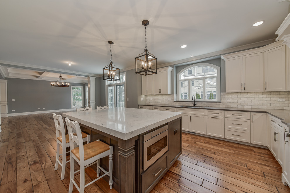 This is an example of a large transitional l-shaped eat-in kitchen in Chicago with a single-bowl sink, white cabinets, quartzite benchtops, grey splashback, stone tile splashback, panelled appliances, with island, shaker cabinets, laminate floors and brown floor.