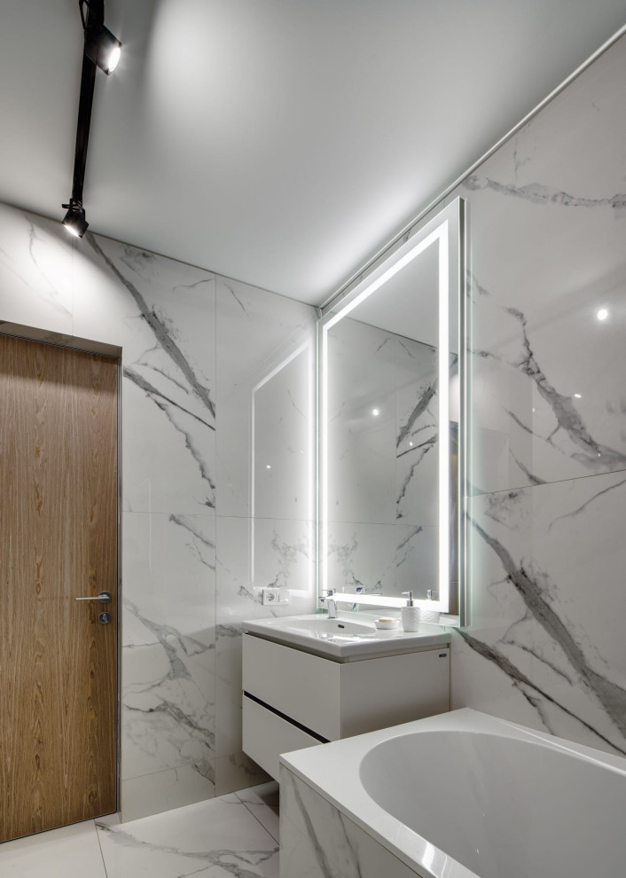 Свежая идея для дизайна: главная, серо-белая ванная комната среднего размера в современном стиле с плоскими фасадами, белыми фасадами, полновстраиваемой ванной, душем над ванной, инсталляцией, белой плиткой, керамогранитной плиткой, белыми стенами, полом из керамогранита, настольной раковиной, белым полом, шторкой для ванной, зеркалом с подсветкой, тумбой под одну раковину и подвесной тумбой - отличное фото интерьера
