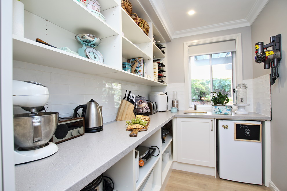 Design ideas for a large eclectic l-shaped kitchen pantry in Sydney with an undermount sink, shaker cabinets, white cabinets, quartz benchtops, white splashback, subway tile splashback, stainless steel appliances, light hardwood floors, with island and brown floor.