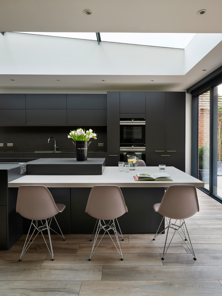 Photo of a contemporary galley eat-in kitchen in Berkshire with a drop-in sink, flat-panel cabinets, black cabinets, copper benchtops, black splashback, black appliances, with island, beige floor and black benchtop.