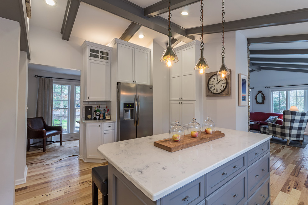 Example of a large transitional u-shaped medium tone wood floor and brown floor enclosed kitchen design with an undermount sink, shaker cabinets, white cabinets, quartzite countertops, white backsplash, subway tile backsplash, stainless steel appliances and an island