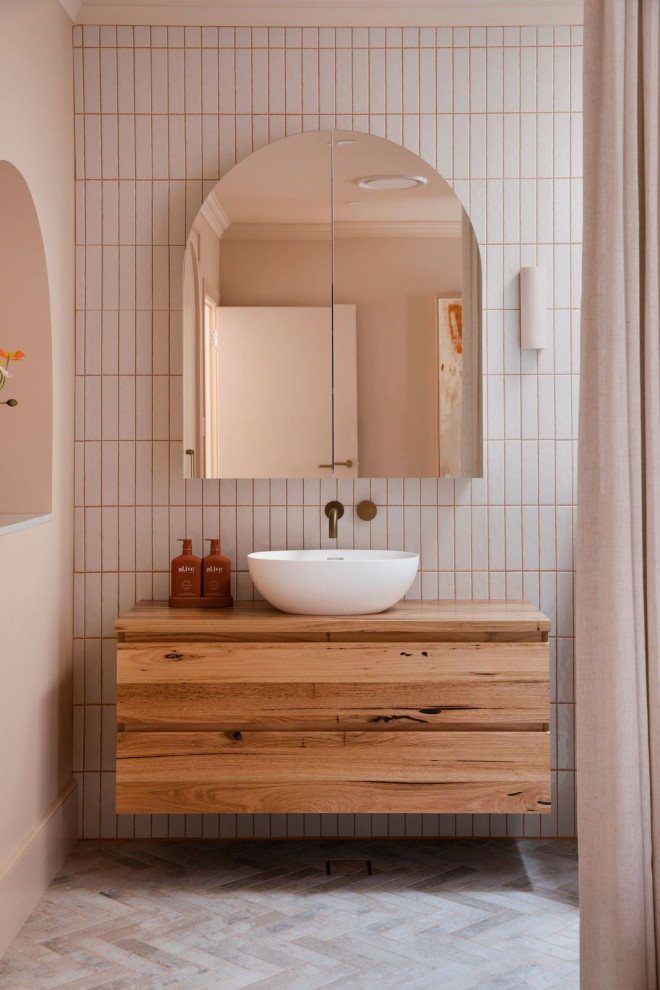 Maritim inredning av ett badrum, med skåp i mellenmörkt trä, en öppen dusch, beige kakel, keramikplattor, beige väggar, klinkergolv i porslin, träbänkskiva, beiget golv och med dusch som är öppen