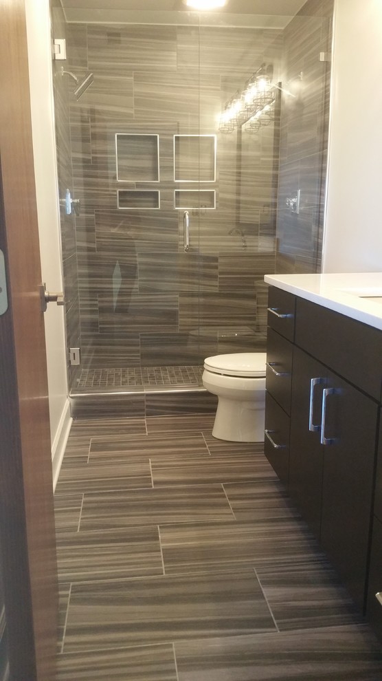 Alcove shower - mid-sized transitional 3/4 brown tile and porcelain tile porcelain tile and brown floor alcove shower idea with flat-panel cabinets, brown cabinets, a two-piece toilet, white walls, an undermount sink, solid surface countertops, a hinged shower door and white countertops