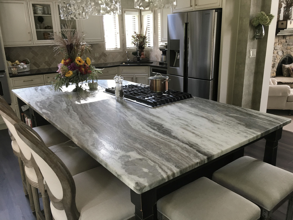 Example of a large transitional u-shaped laminate floor and gray floor eat-in kitchen design with an undermount sink, recessed-panel cabinets, white cabinets, granite countertops, white backsplash, ceramic backsplash, stainless steel appliances, an island and black countertops