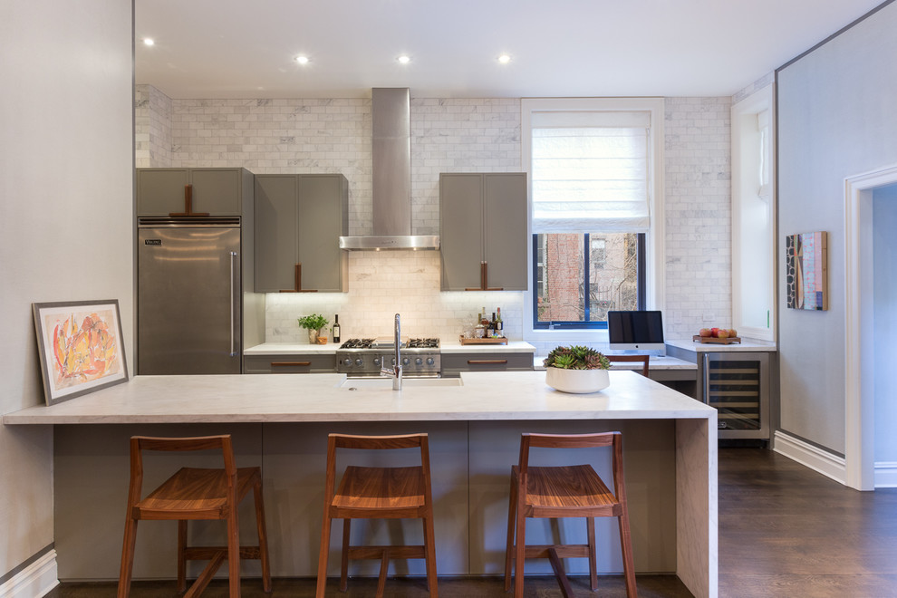 Mid-sized contemporary galley separate kitchen in New York with a farmhouse sink, flat-panel cabinets, grey cabinets, marble benchtops, white splashback, ceramic splashback, stainless steel appliances, medium hardwood floors, a peninsula and brown floor.