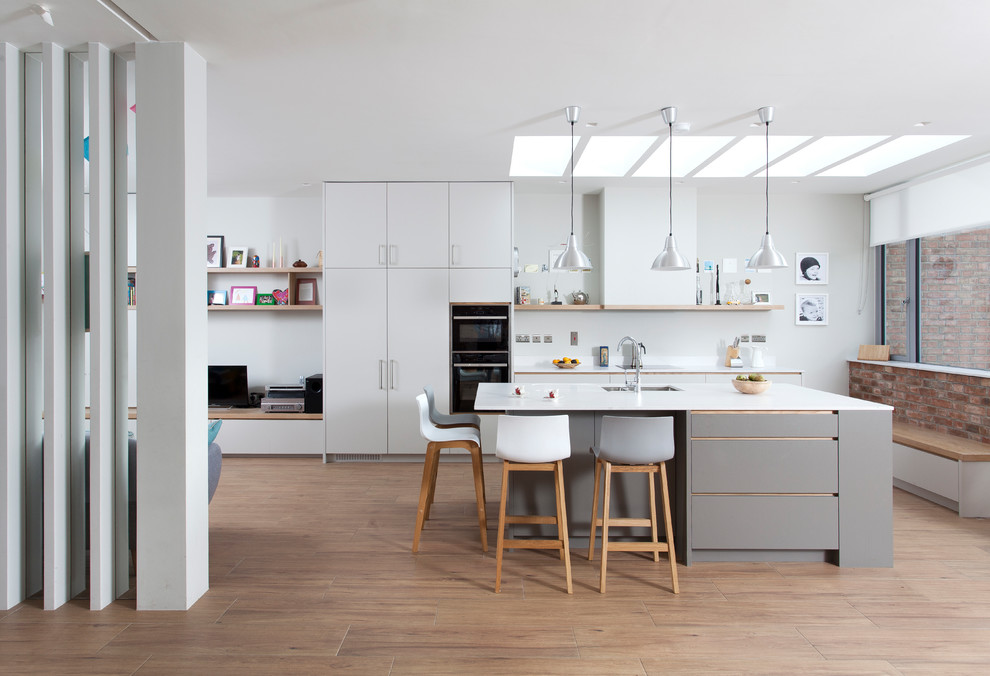 Mid-sized contemporary single-wall open plan kitchen in Dublin with flat-panel cabinets, white splashback, black appliances, laminate floors, with island, an undermount sink, white cabinets and brown floor.