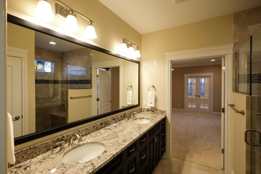 Large transitional master beige floor alcove shower photo with raised-panel cabinets, brown cabinets, beige walls, an undermount sink, granite countertops, a hinged shower door and gray countertops