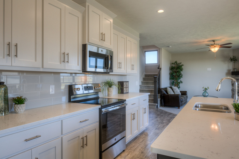 Open concept kitchen - open concept kitchen idea in Omaha with white cabinets, quartz countertops, gray backsplash, ceramic backsplash, stainless steel appliances and an island