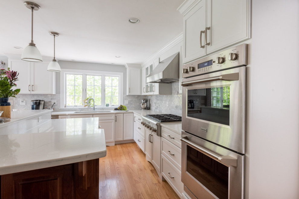 Inspiration for a large transitional l-shaped medium tone wood floor, brown floor and coffered ceiling eat-in kitchen remodel in Boston with an undermount sink, shaker cabinets, white cabinets, quartz countertops, gray backsplash, subway tile backsplash, stainless steel appliances, an island and white countertops