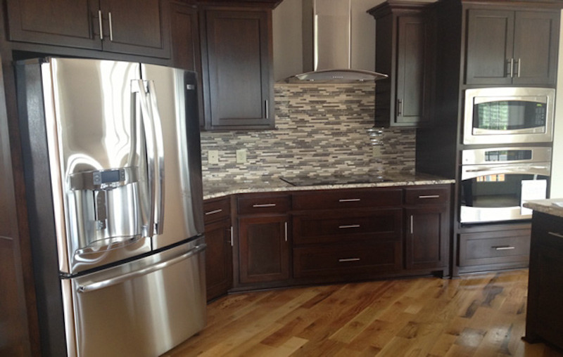 Kitchen - large medium tone wood floor kitchen idea with recessed-panel cabinets, dark wood cabinets and stainless steel appliances
