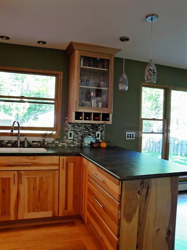 Eat-in kitchen - mid-sized rustic l-shaped light wood floor eat-in kitchen idea with an integrated sink, shaker cabinets, light wood cabinets, solid surface countertops, glass tile backsplash, black appliances, a peninsula and brown countertops