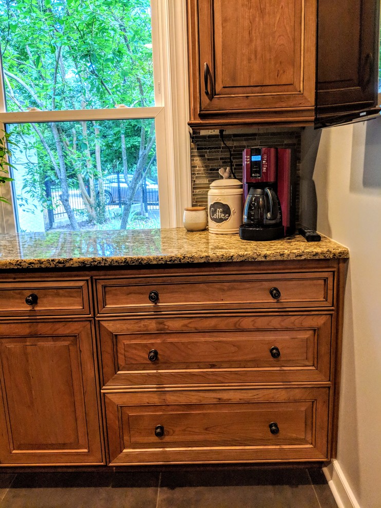 Inspiration for a mid-sized transitional u-shaped porcelain tile and black floor kitchen remodel with a farmhouse sink, raised-panel cabinets, light wood cabinets, granite countertops, green backsplash, glass sheet backsplash, stainless steel appliances, an island and brown countertops