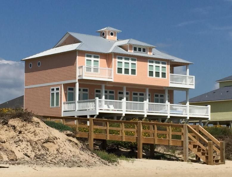 Photo of a large beach style three-storey orange house exterior in Houston with vinyl siding and a metal roof.