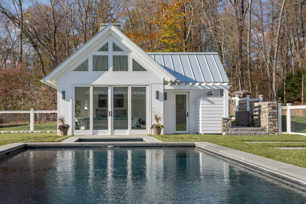 Mid-sized country backyard rectangular lap pool in New York with a pool house and natural stone pavers.