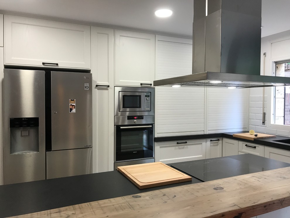 This is an example of a large eclectic u-shaped open plan kitchen in Barcelona with a double-bowl sink, beaded inset cabinets, white cabinets, granite benchtops, white splashback, ceramic splashback, stainless steel appliances, marble floors, with island, white floor and black benchtop.