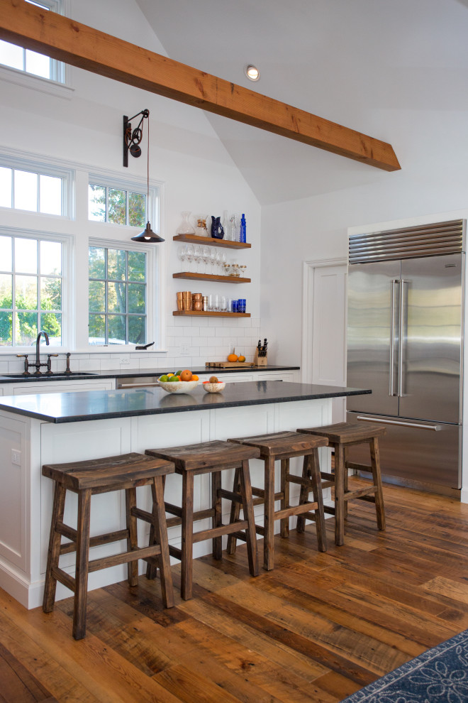 Inspiration for a mid-sized country l-shaped kitchen in Boston with an undermount sink, shaker cabinets, white cabinets, quartzite benchtops, white splashback, subway tile splashback, stainless steel appliances, medium hardwood floors, with island, brown floor, black benchtop and exposed beam.
