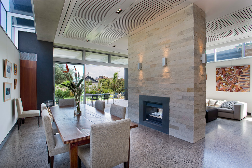Photo of a large open plan dining in Sydney with beige walls, concrete floors, a two-sided fireplace, a stone fireplace surround and grey floor.