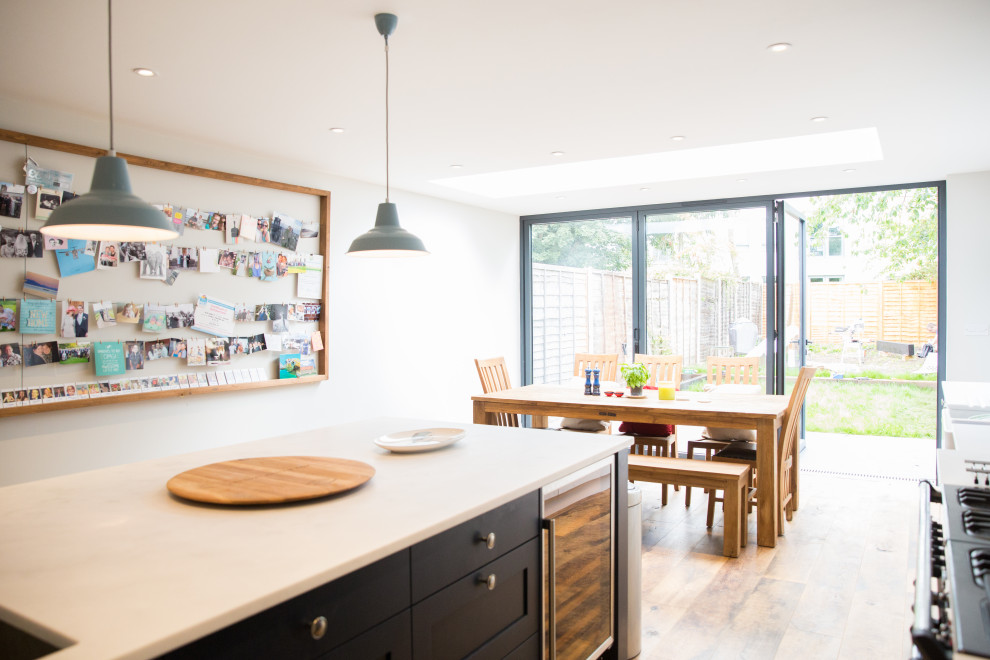 Design ideas for a mid-sized modern l-shaped open plan kitchen in London with an undermount sink, shaker cabinets, blue cabinets, solid surface benchtops, black appliances, dark hardwood floors, with island, brown floor and white benchtop.