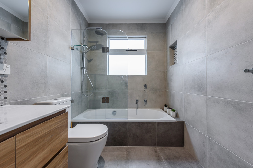 Mid-sized modern bathroom in Melbourne with furniture-like cabinets, light wood cabinets, a drop-in tub, a shower/bathtub combo, multi-coloured tile, porcelain tile, grey walls, ceramic floors, marble benchtops, grey floor and white benchtops.
