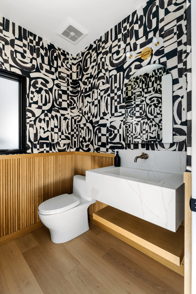 Réalisation d'un WC et toilettes design avec WC à poser, un mur multicolore, un sol en bois brun, un lavabo intégré, un sol marron, un plan de toilette blanc, meuble-lavabo suspendu, boiseries et du papier peint.