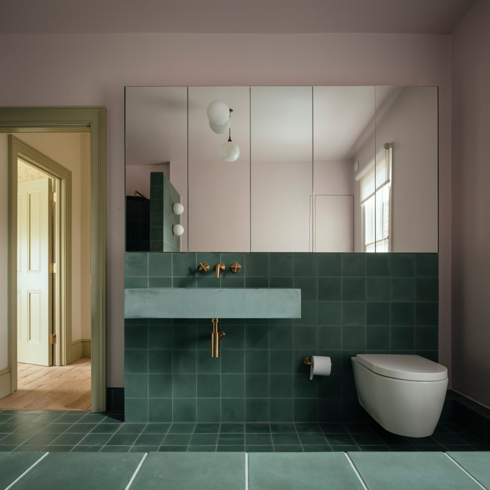 Design ideas for a medium sized contemporary bathroom in London with a wall mounted toilet, green tiles, cement tiles, cement flooring, concrete worktops, green floors, green worktops, a single sink, a floating vanity unit, pink walls and a wall-mounted sink.