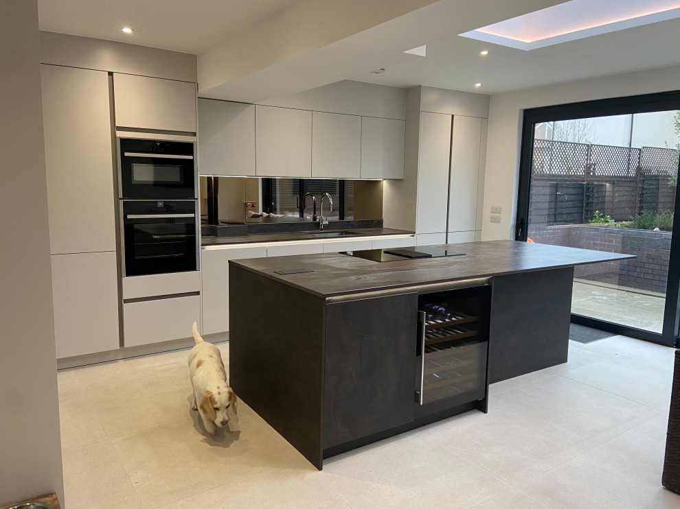 Photo of a large contemporary galley kitchen in London with quartz worktops, mirror splashback, recessed-panel cabinets, grey cabinets, porcelain flooring, an island and white floors.