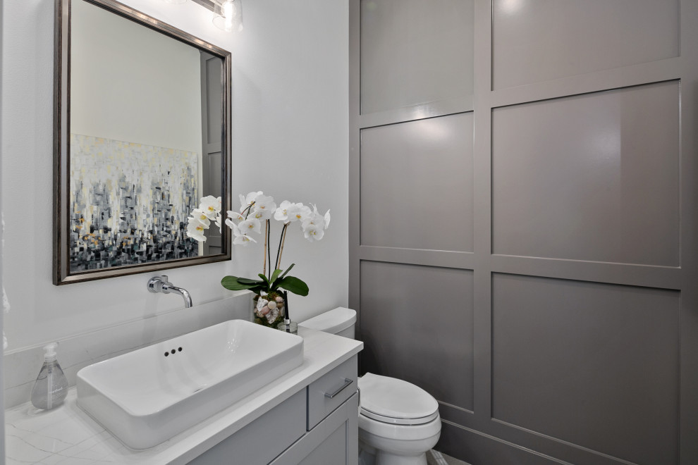 Design ideas for a mid-sized country powder room in Seattle with recessed-panel cabinets, grey cabinets, a two-piece toilet, grey walls, a vessel sink, engineered quartz benchtops, white benchtops, a built-in vanity and decorative wall panelling.