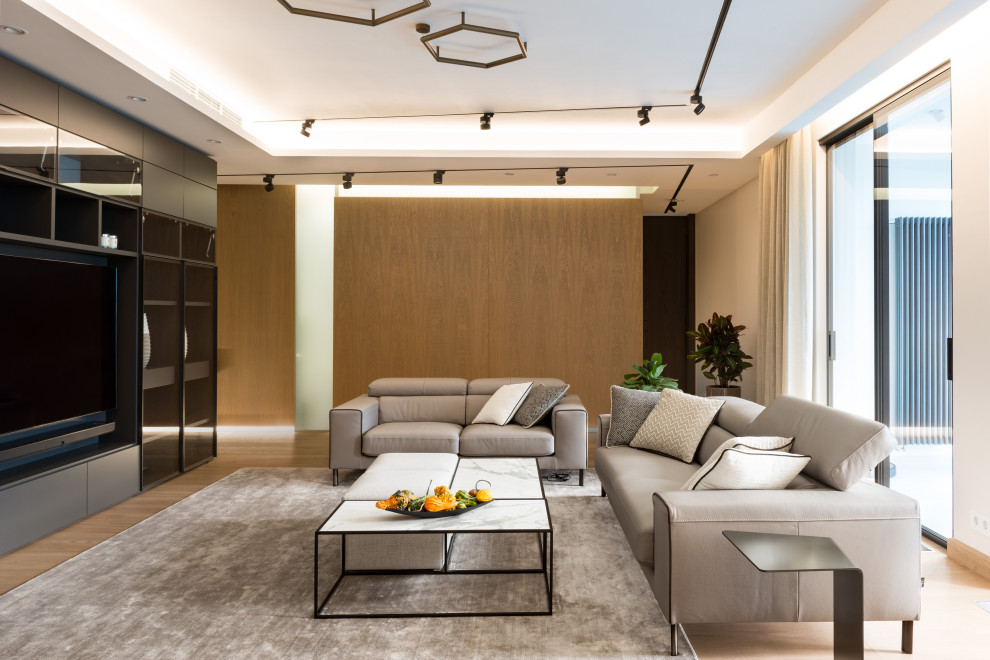 Ejemplo de salón abierto actual de tamaño medio con paredes grises, suelo de madera en tonos medios, televisor colgado en la pared y bandeja