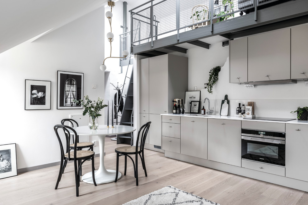 This is an example of a mid-sized industrial single-wall eat-in kitchen in Gothenburg with a single-bowl sink, flat-panel cabinets, grey cabinets, marble benchtops, light hardwood floors and no island.