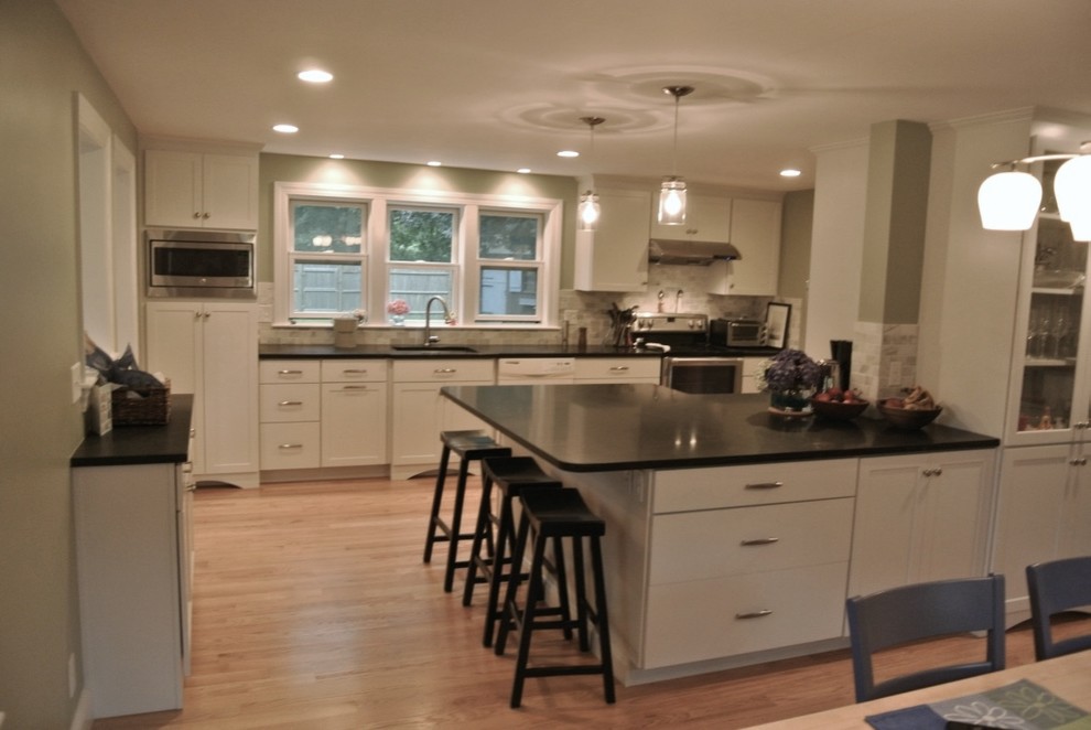 Transitional u-shaped light wood floor eat-in kitchen photo in Boston with an undermount sink, shaker cabinets, white cabinets, beige backsplash, porcelain backsplash, stainless steel appliances, a peninsula and black countertops