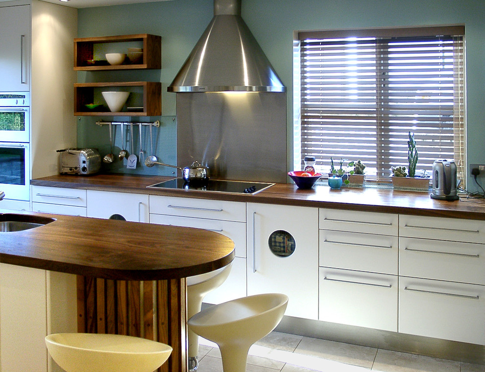 This is an example of a contemporary kitchen/diner with an integrated sink, flat-panel cabinets, wood worktops, stainless steel appliances, travertine flooring and an island.