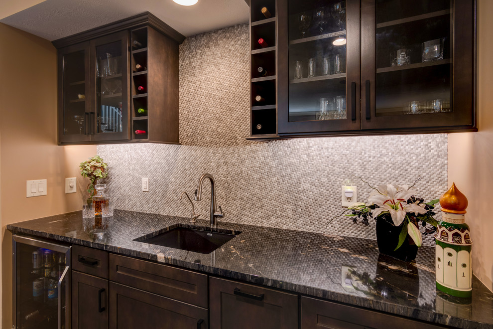 Photo of a mid-sized arts and crafts single-wall wet bar in Indianapolis with a drop-in sink, shaker cabinets, dark wood cabinets, granite benchtops, grey splashback, stone tile splashback, dark hardwood floors, brown floor and black benchtop.