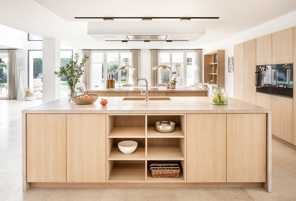 Mid-sized contemporary u-shaped open plan kitchen in Palma de Mallorca with flat-panel cabinets, light wood cabinets, black appliances, multiple islands, beige floor and beige benchtop.