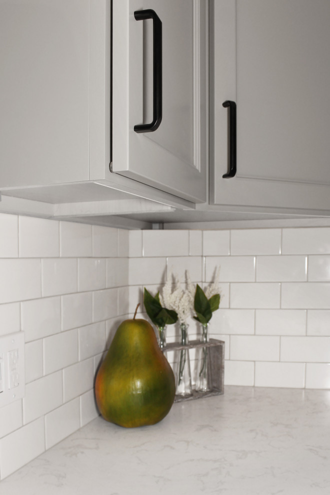 Inspiration for a large transitional u-shaped light wood floor and brown floor enclosed kitchen remodel in Boston with a double-bowl sink, shaker cabinets, gray cabinets, quartz countertops, white backsplash, porcelain backsplash, black appliances, an island and white countertops