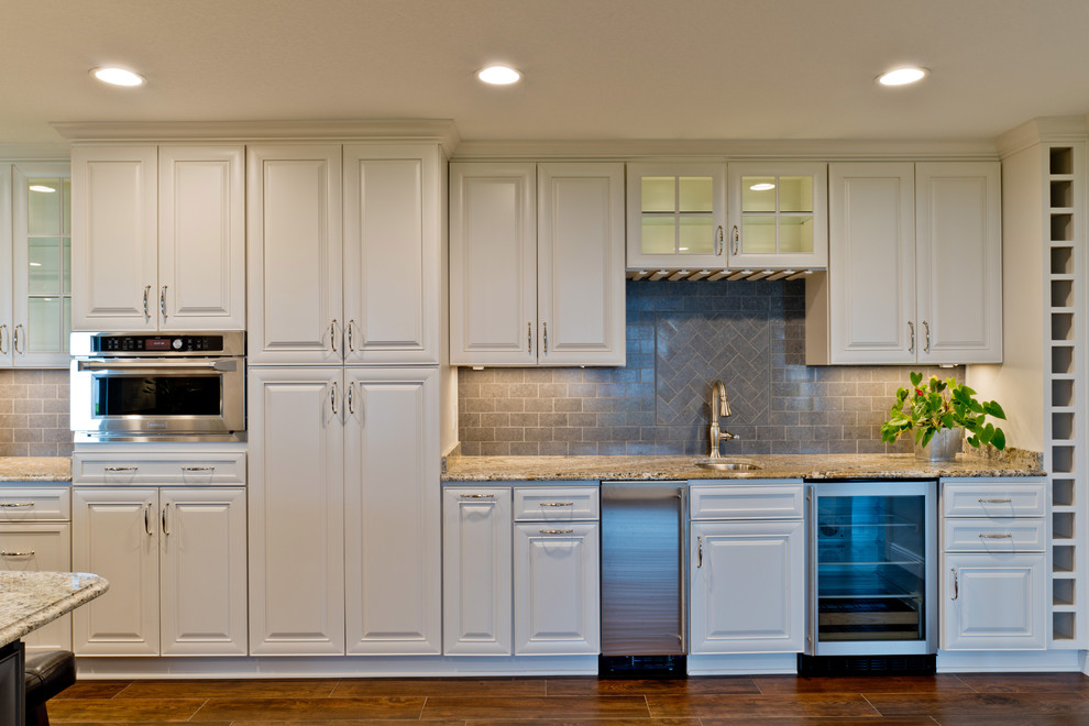 Eat-in kitchen - large transitional galley porcelain tile eat-in kitchen idea in Miami with an undermount sink, raised-panel cabinets, white cabinets, granite countertops, gray backsplash, porcelain backsplash, stainless steel appliances and an island