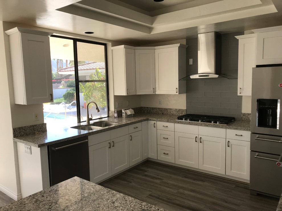 Open concept kitchen - huge transitional u-shaped laminate floor and gray floor open concept kitchen idea with shaker cabinets, white cabinets, granite countertops, a peninsula, an undermount sink, gray backsplash, subway tile backsplash, stainless steel appliances and gray countertops