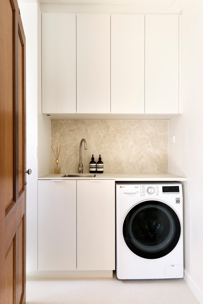 Idéer för en liten skandinavisk beige linjär tvättstuga enbart för tvätt, med en undermonterad diskho, släta luckor, vita skåp, bänkskiva i kvarts, beige stänkskydd, stänkskydd i porslinskakel, vita väggar, klinkergolv i porslin, en tvättmaskin och torktumlare bredvid varandra och brunt golv