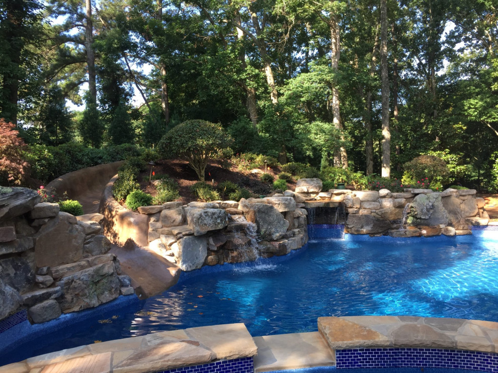 Diseño de piscina natural tradicional grande a medida en patio trasero con paisajismo de piscina