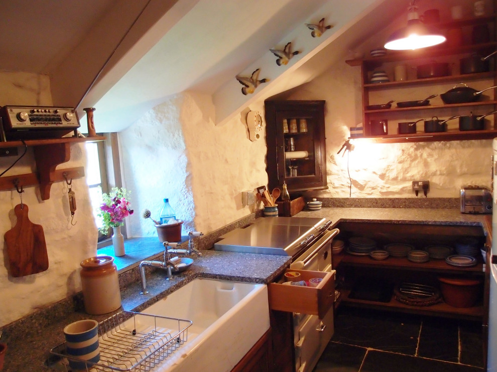 This is an example of a small rustic u-shaped enclosed kitchen in Cornwall with a belfast sink, shaker cabinets, dark wood cabinets, granite worktops, white appliances, slate flooring, no island, grey floors, grey worktops and exposed beams.